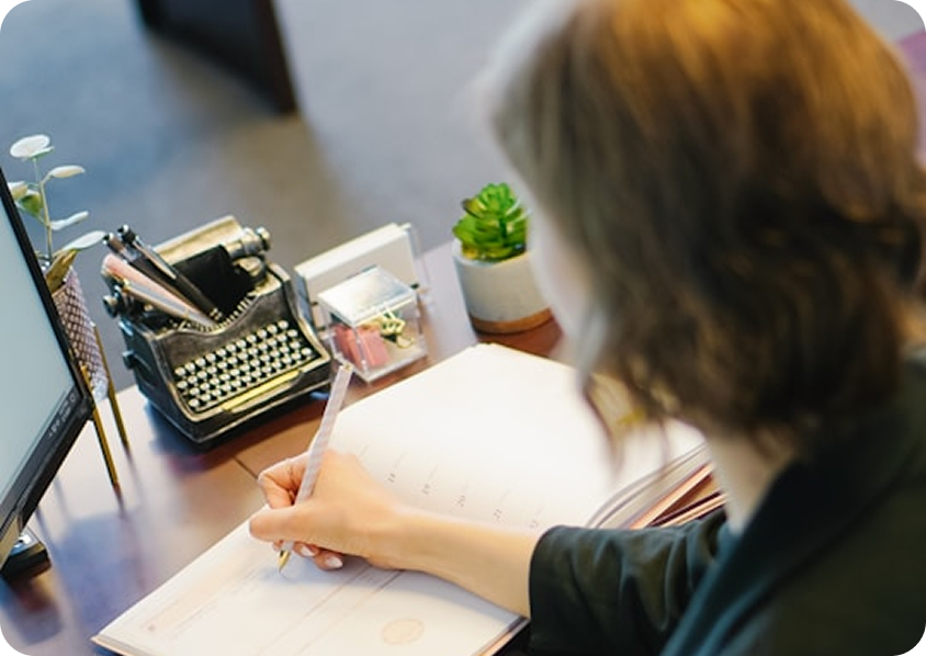 Person writing on a notebook with a laptop nearby